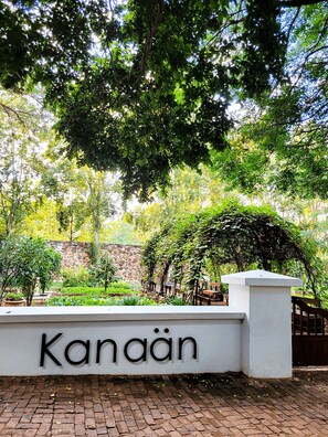Una pared blanca con el nombre 'Kanaän' en letras negras, una pared de piedra y un sendero de ladrillos.