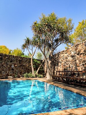 A swimming pool with a stone wall and a wooden deck. - Kleinkaap Boutique Hotel (Centurion)