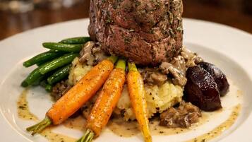 A plated dish with a beef center, garnished with greens, accompanied by carrots and green beans.