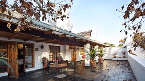 A courtyard with a wooden table and chairs, potted plants, and a tiled floor with scattered leaves. - Kleinkaap Boutique Hotel (Centurion)