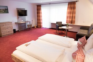 Een hotelkamer met een bed, een bureau met stoel, een aan de muur bevestigde televisie en een raam met gordijnen.