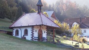 A small chapel with a tiled roof and a bell tower, surrounded by a grassy area and trees.