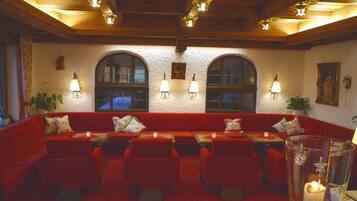 A cozy interior with a red sofa and chairs, arched windows, and wall-mounted lamps.