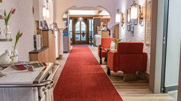 A hotel lobby with a red carpet, wooden beams, a reception desk, and seating areas.