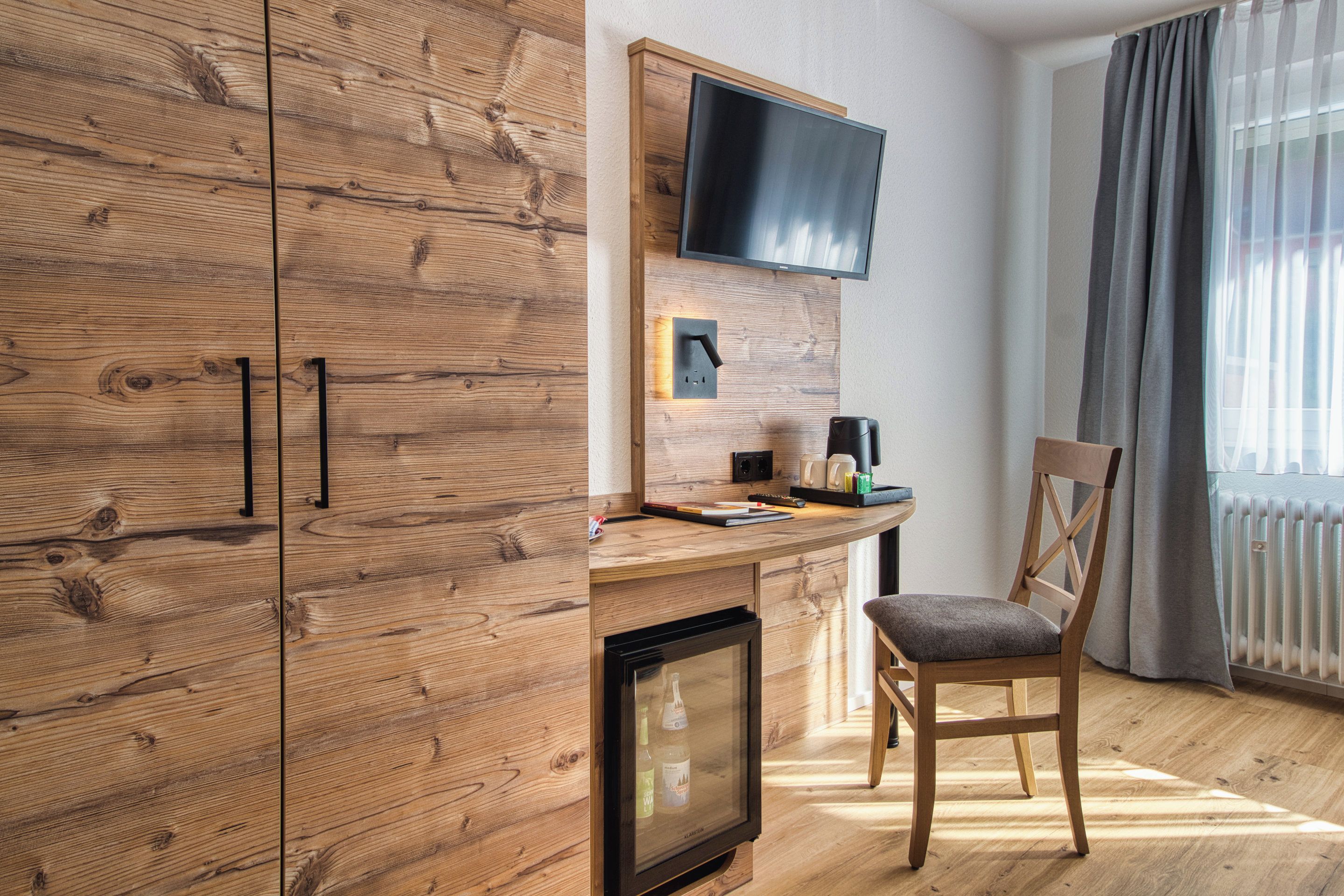 Ein modernes Zimmer mit Holzausstattung, einem Flachbildfernseher an der Wand, einem kleinen Tisch mit Stuhl und einer Heizung.