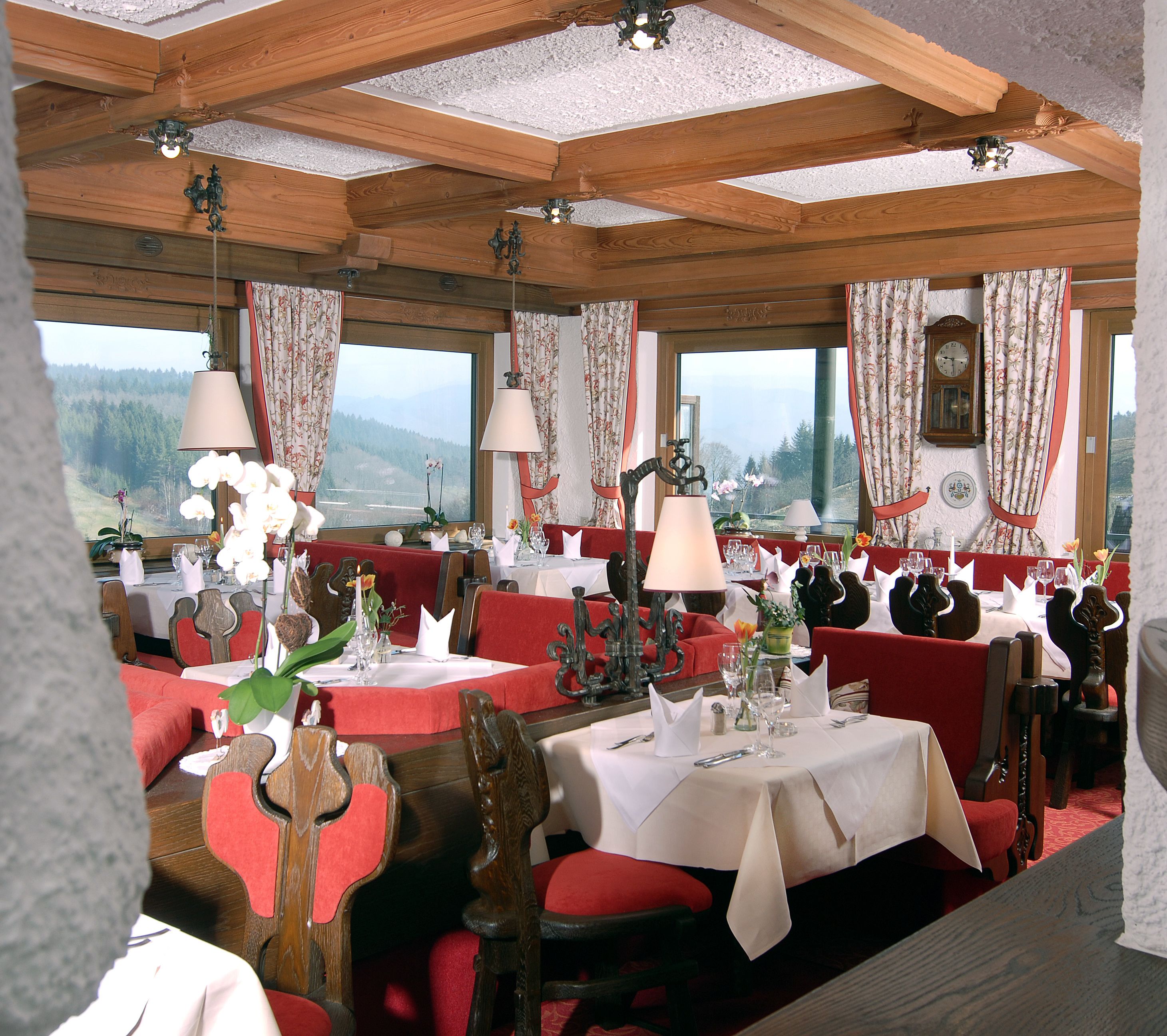 A restaurant with wooden beams, red upholstered chairs, and tables set for dining.