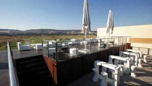 Terraço no telhado com mobiliário de jardim branco, guarda-sóis e vista para um campo de golfe.