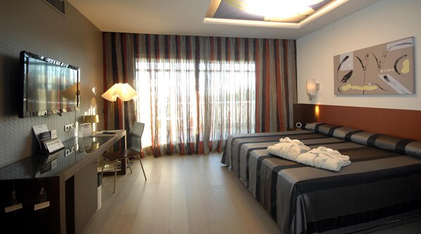 A hotel room with a bed, a desk with a lamp, a television, and a large window with curtains. - Sercotel El Encin Golf (Alcala de Henares)