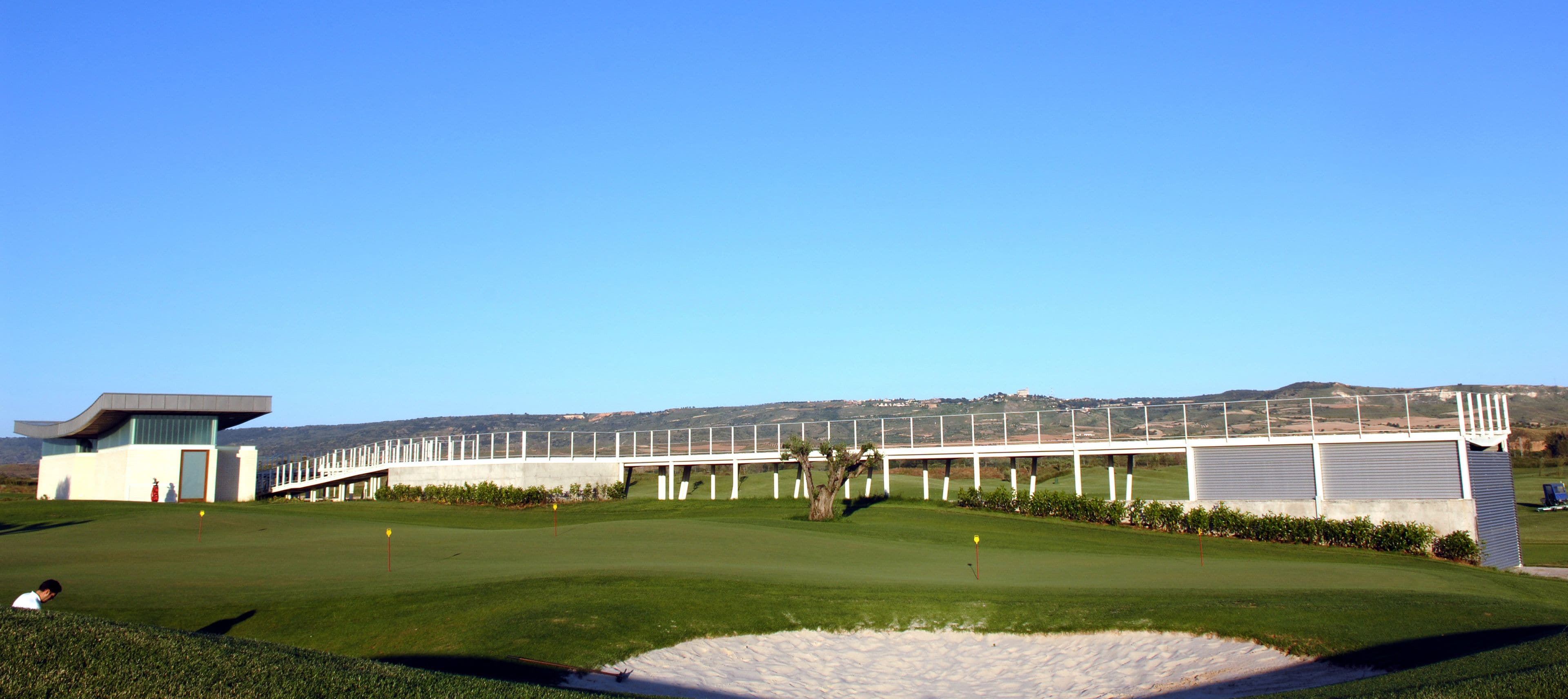 A modern golf course with a clubhouse, a bridge, and a scenic view of hills in the background.