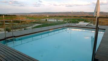 Una piscina con cubierta de madera, barandilla de metal y vistas al campo.