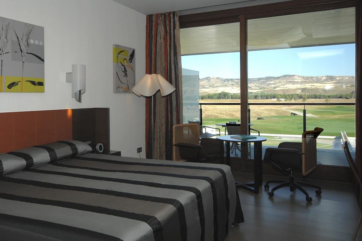 A hotel room with a large bed, a desk, and a view of a golf course.