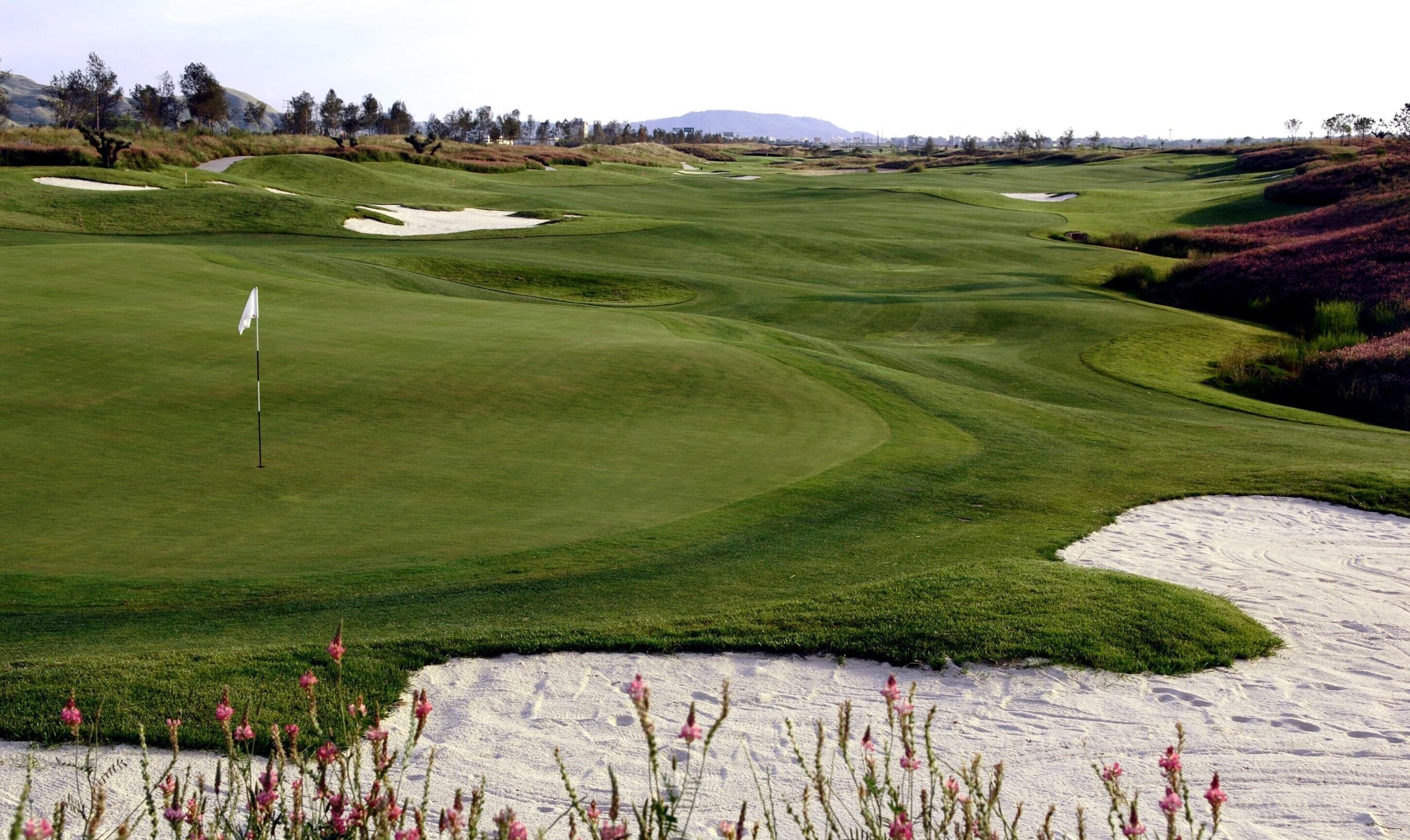 A golf course with sand bunkers, a flagstick, and a distant mountain range.