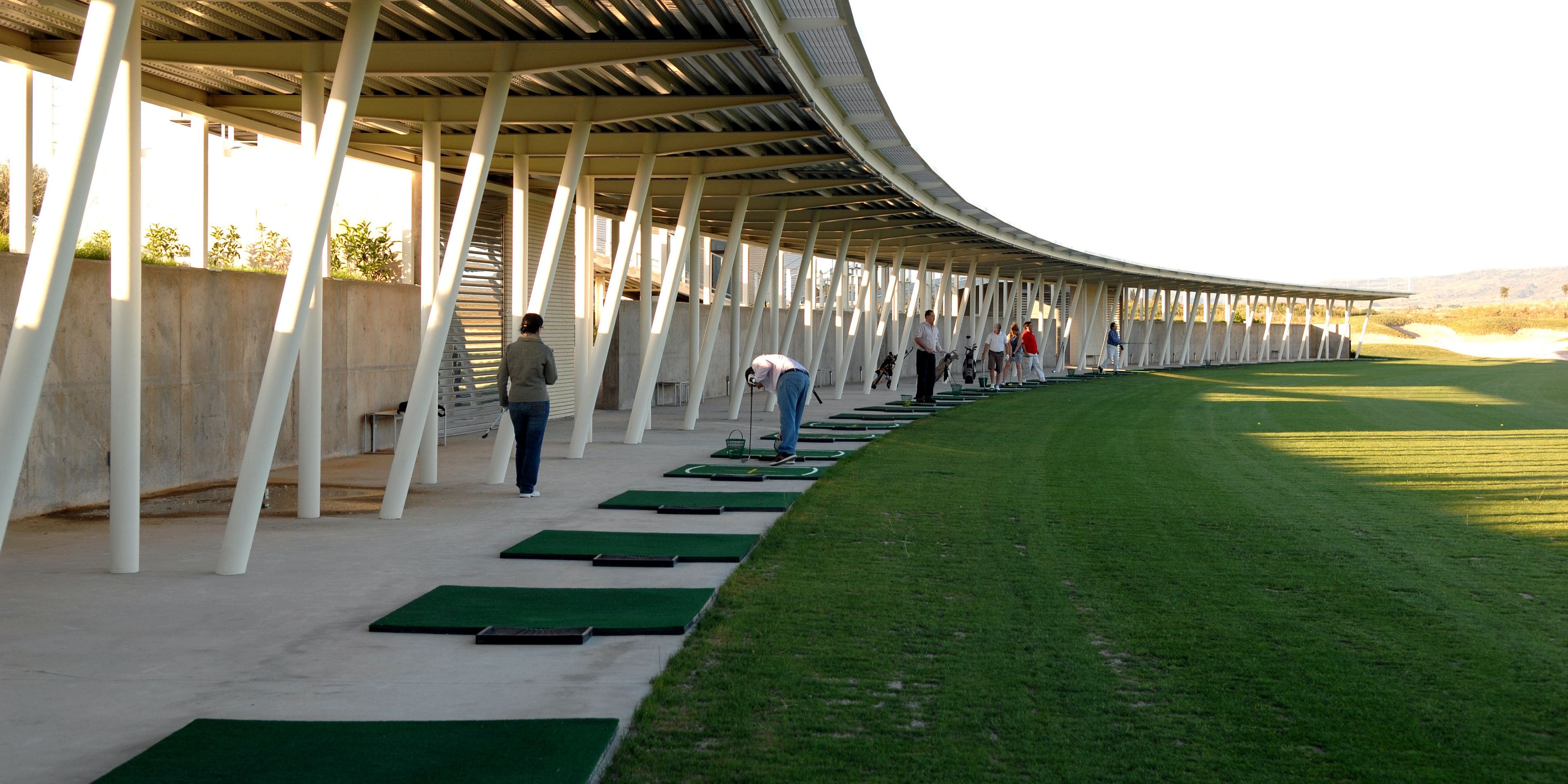 A covered outdoor area with a curved roof, green artificial turf, and white pillars.