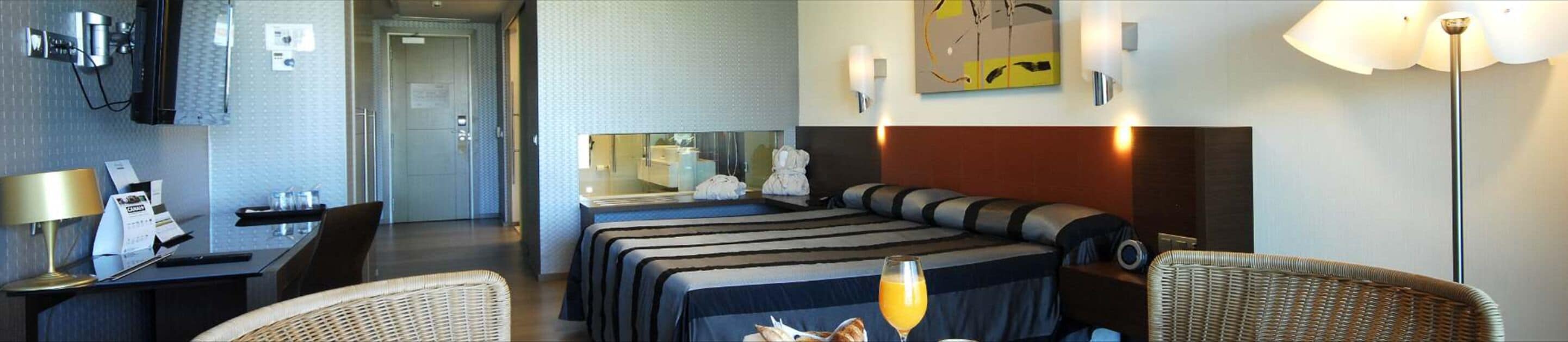 Una habitación de hotel con una cama, un escritorio con lámpara, una silla y una mesita de noche.