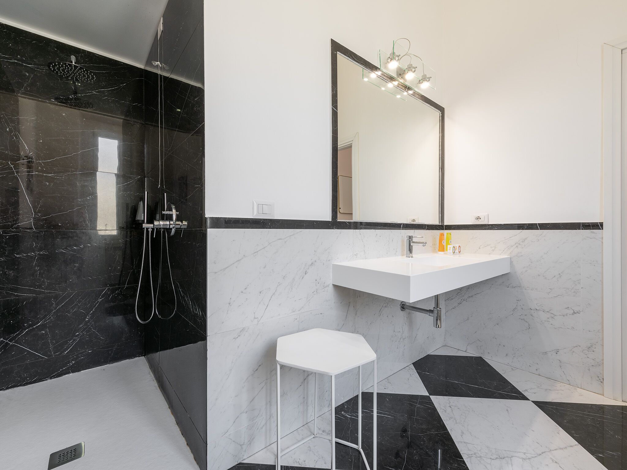 A modern bathroom with a black and white marble design, a white sink, and a mirror with lights above it.