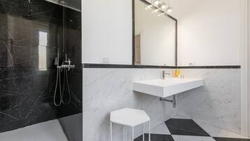 A modern bathroom with a black and white marble design, a white sink, and a mirror with lights above it.