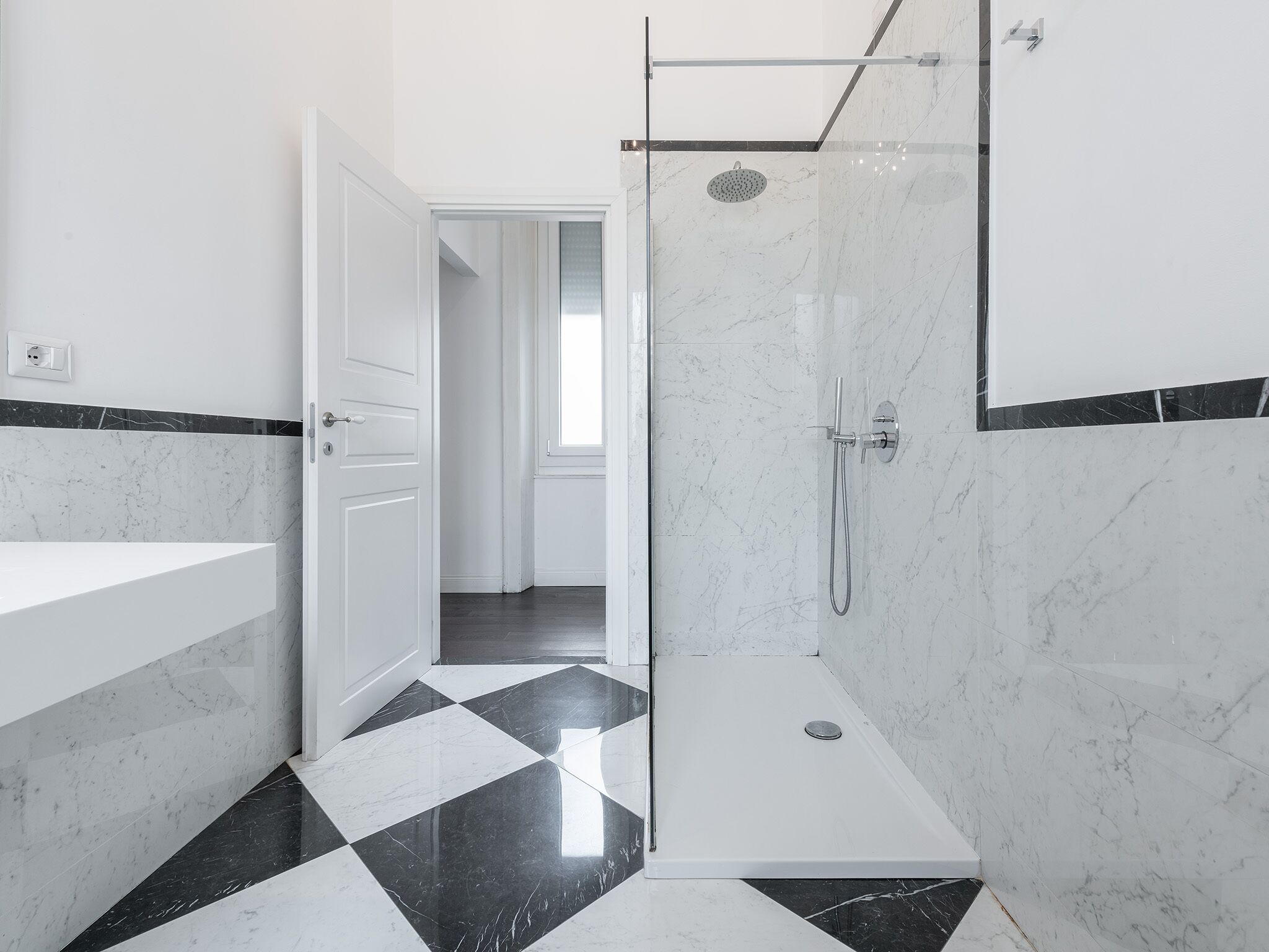 A modern bathroom with a shower, a white sink, and a checkered floor.