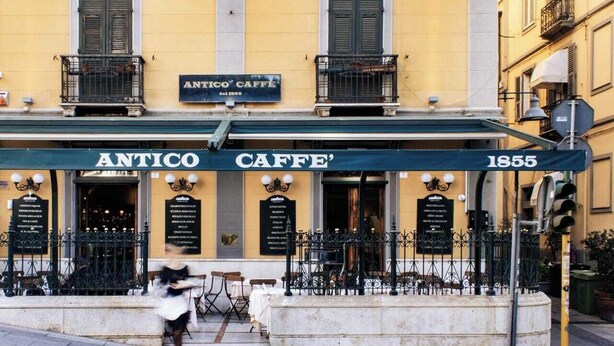 A building with a sign reading "ANTICO CAFFE' 1855" and outdoor seating with tables and chairs.