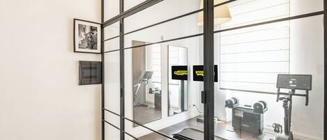 A gym with exercise equipment, a treadmill, and a mirrored wall with the word 'HERITAGE' visible.