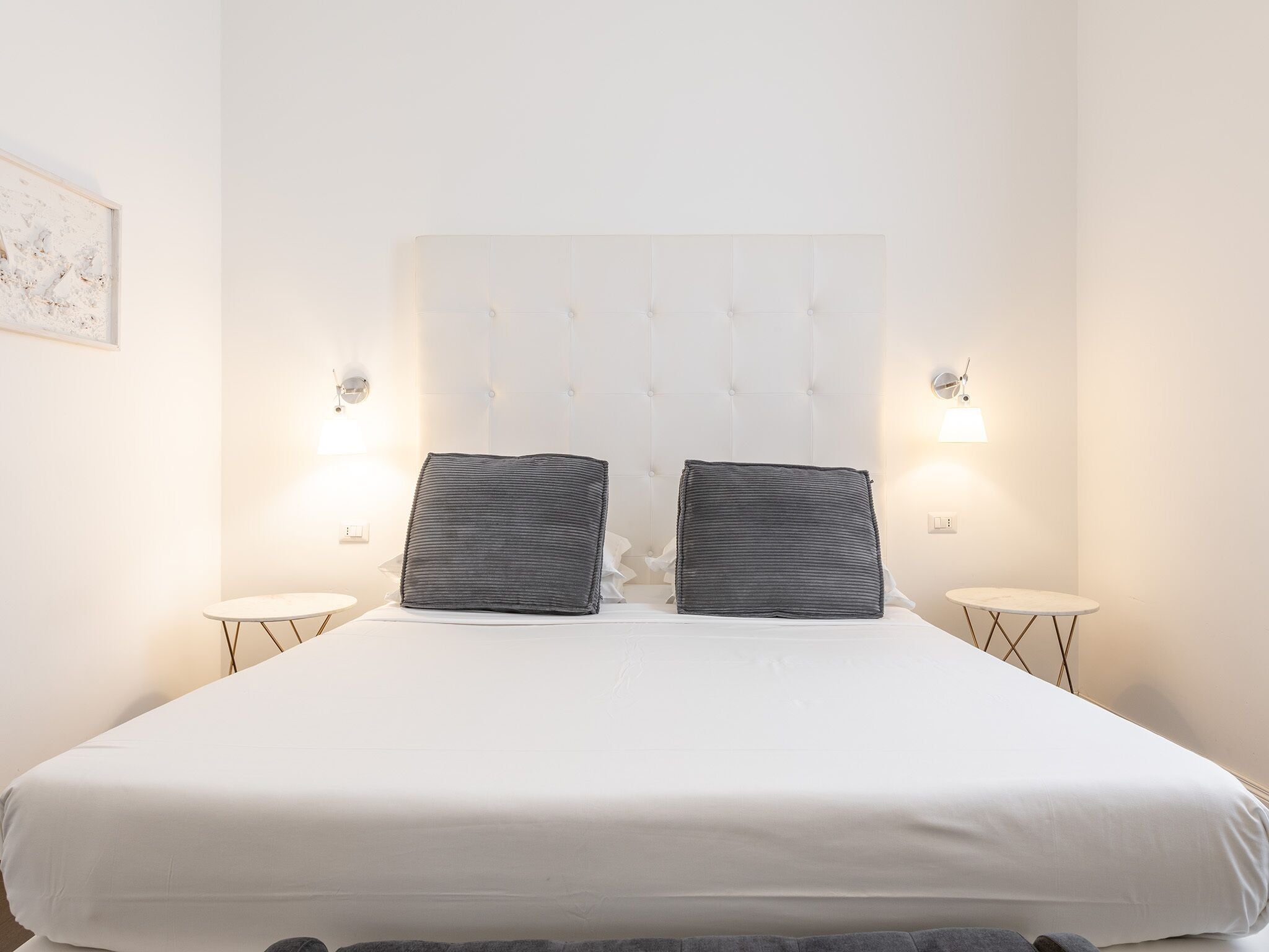 A neatly made bed with a tufted headboard, two bedside lamps, and a small round table.