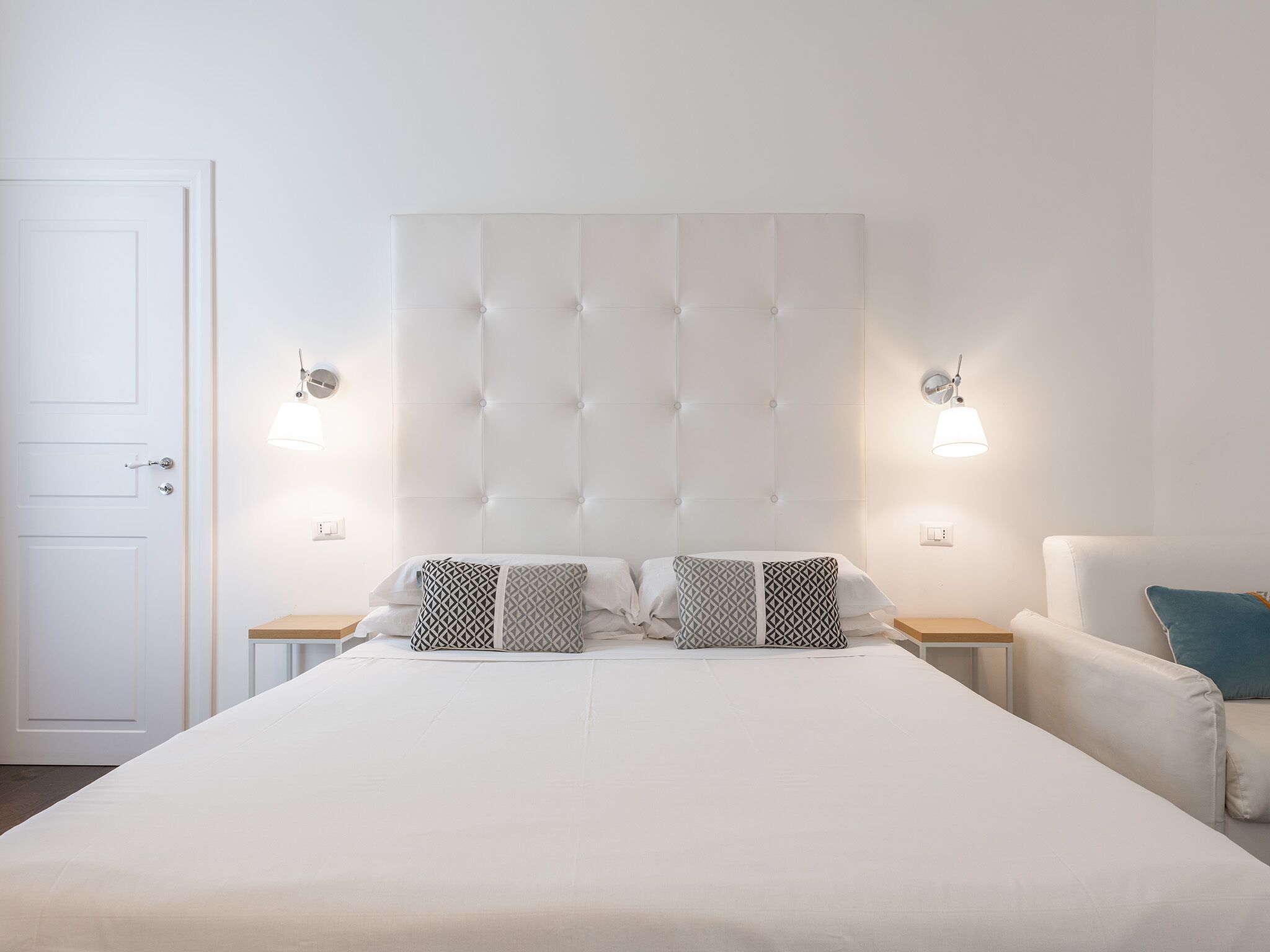 A bedroom with a large bed, two bedside tables, a chair, and a white door.