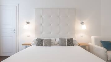 A bedroom with a large bed, two bedside tables, a chair, and a white door.