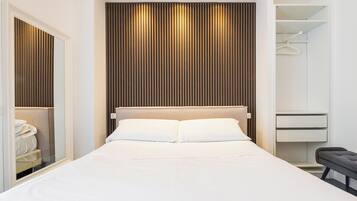 A modern bedroom with a large bed, a wooden slatted headboard, a walk-in closet, and a bench by the bed.