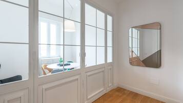 A room with a large window, a round table with chairs, and a wall-mounted mirror.