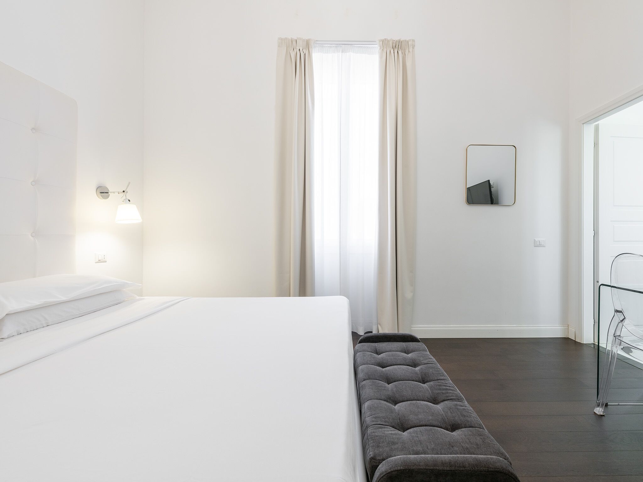 Una camera d'hotel moderna con un letto rifatto, una panca, una lampada a parete e uno specchio.