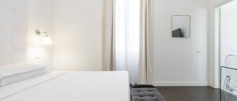 Ein modernes Hotelzimmer mit einem ordentlich bezogenen Bett, einer Bank, einer Wandleuchte und einem Spiegel.