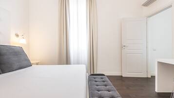 Ein Schlafzimmer mit Bett, Nachttisch, Lampe, Fenster mit Vorhängen und einer Tür.