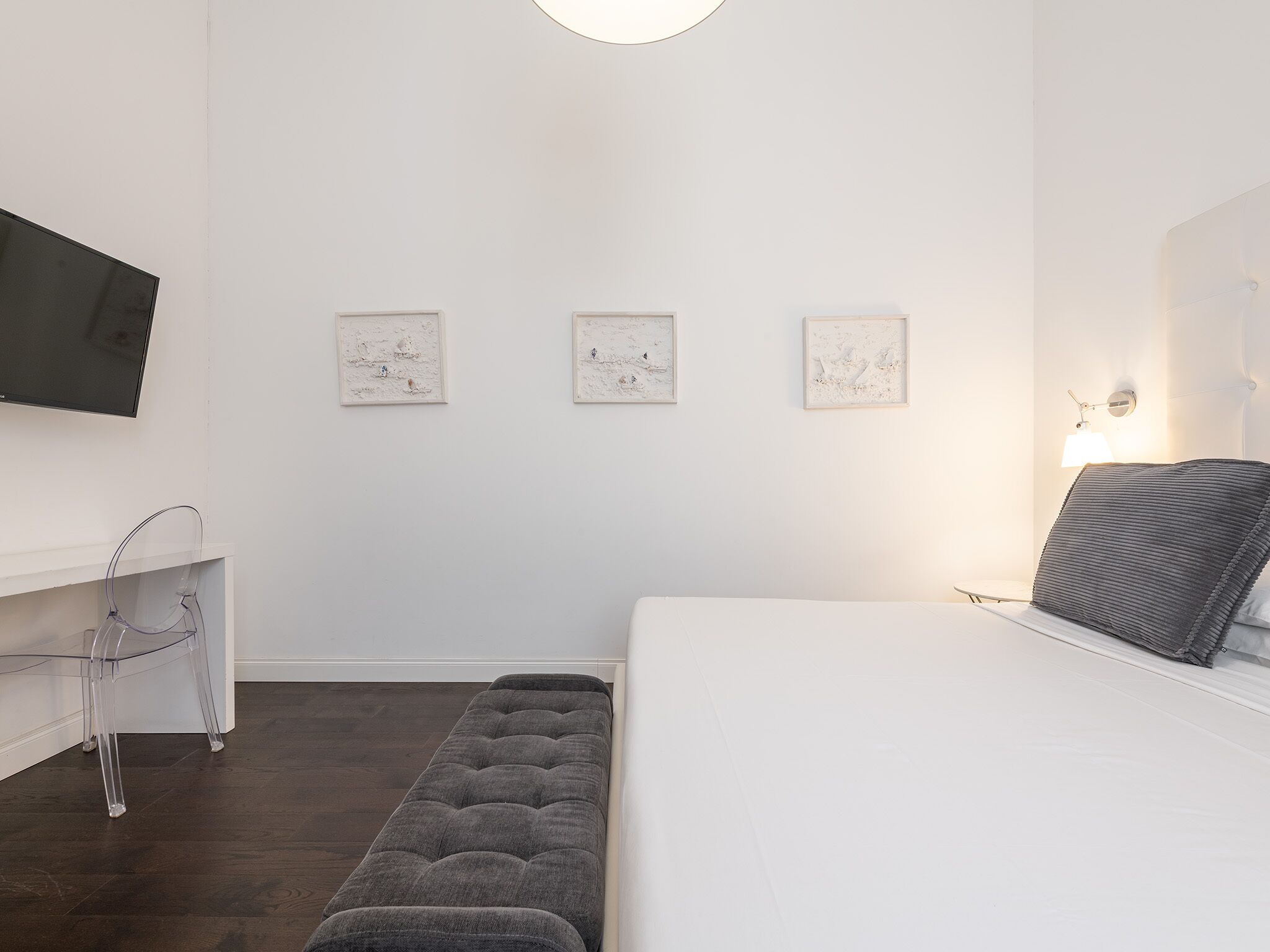 Una habitación de hotel moderna con una cama grande, un televisor montado en la pared y tres cuadros enmarcados.