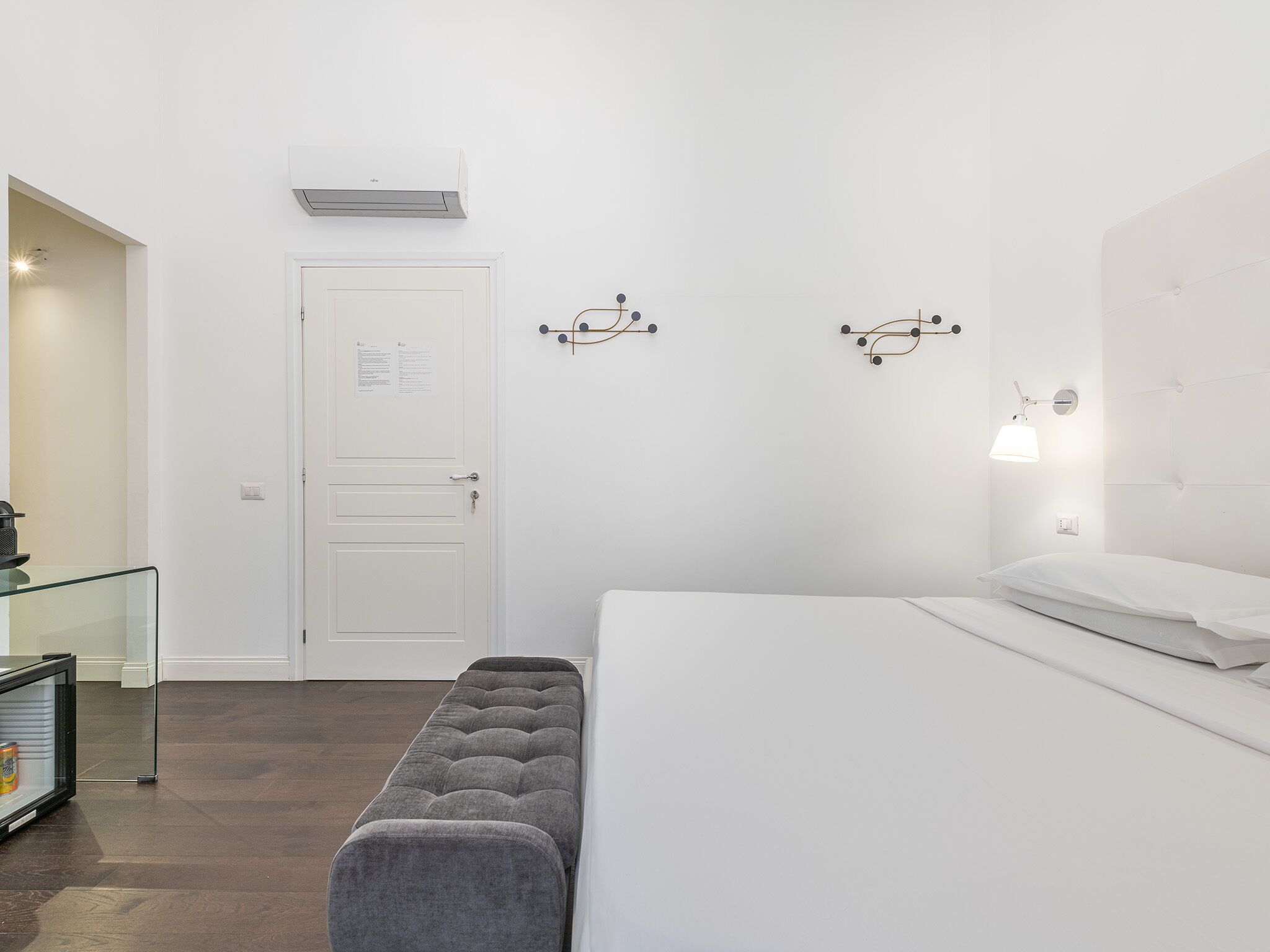A minimalist hotel room with a bed, bench, and wall-mounted light fixtures.