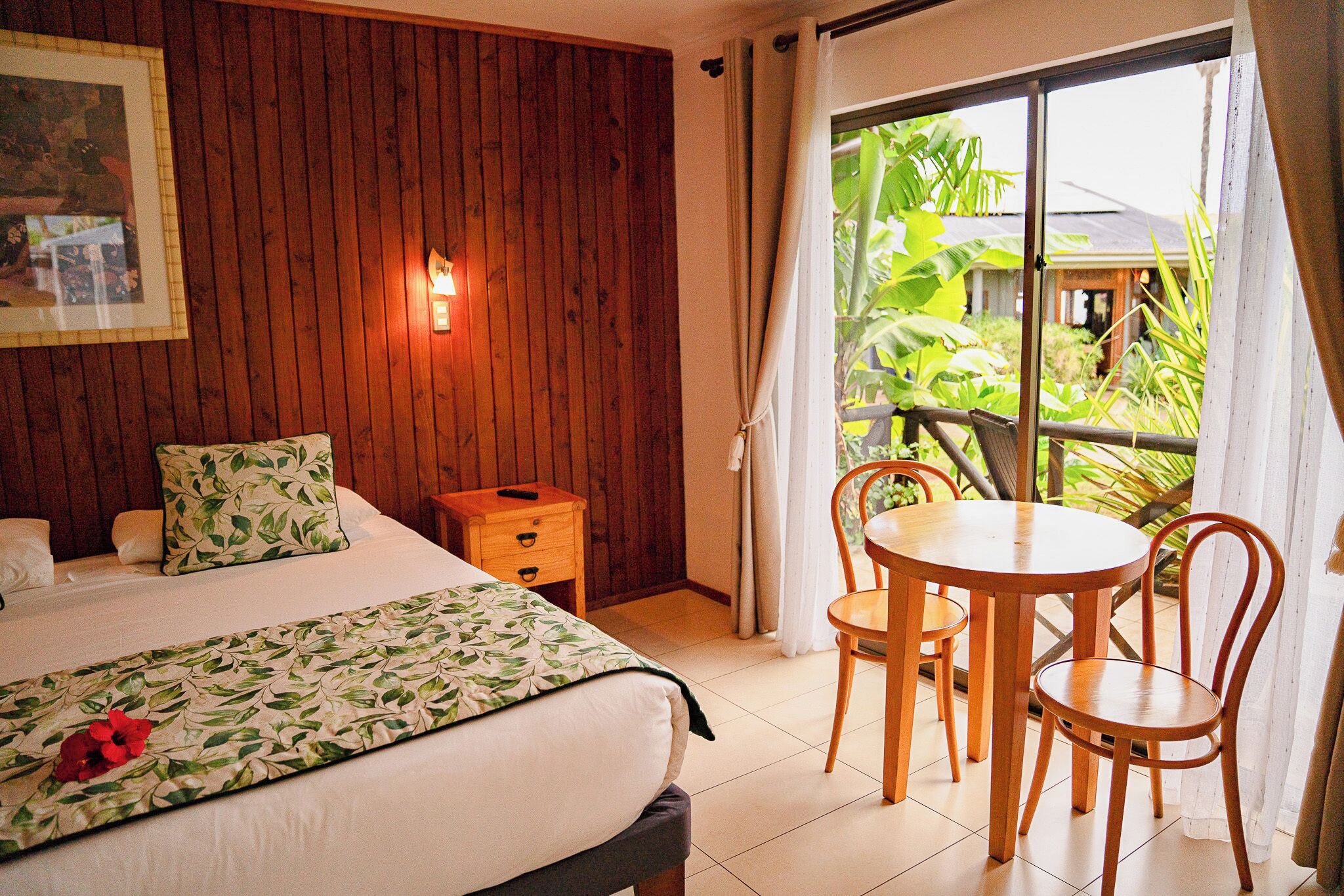 A bedroom with a bed, bedside table, and a view of the outdoors through a window.