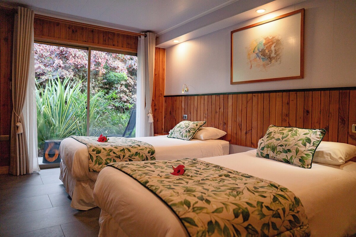 Habitación de hotel con dos camas, un ventanal con cortinas, un panel de pared de madera y un cuadro enmarco.
