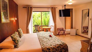 Habitación de hotel con cama, una mesita, sillas, televisión y balcón con plantas.