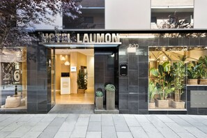 A hotel entrance with a modern facade, a visible reception area, and potted plants outside. - Hotel Acta Laumon (Barcelona)