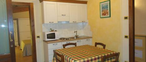 A compact kitchen with white cabinets, a microwave, and a stove. There is a table with a checkered tablecloth and wooden chairs.