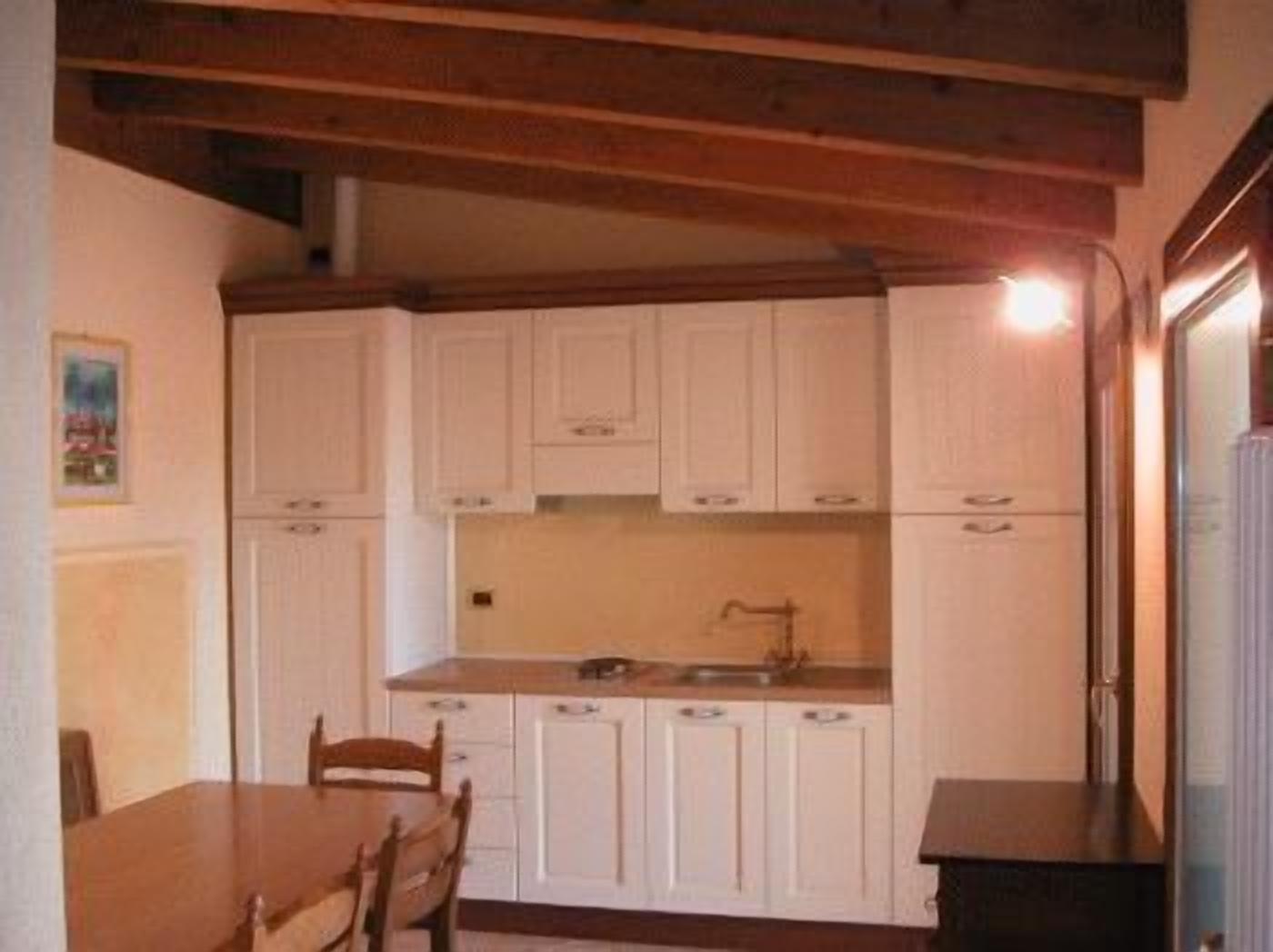 Una cocina compacta con muebles blancos, una mesa de madera y sillas.