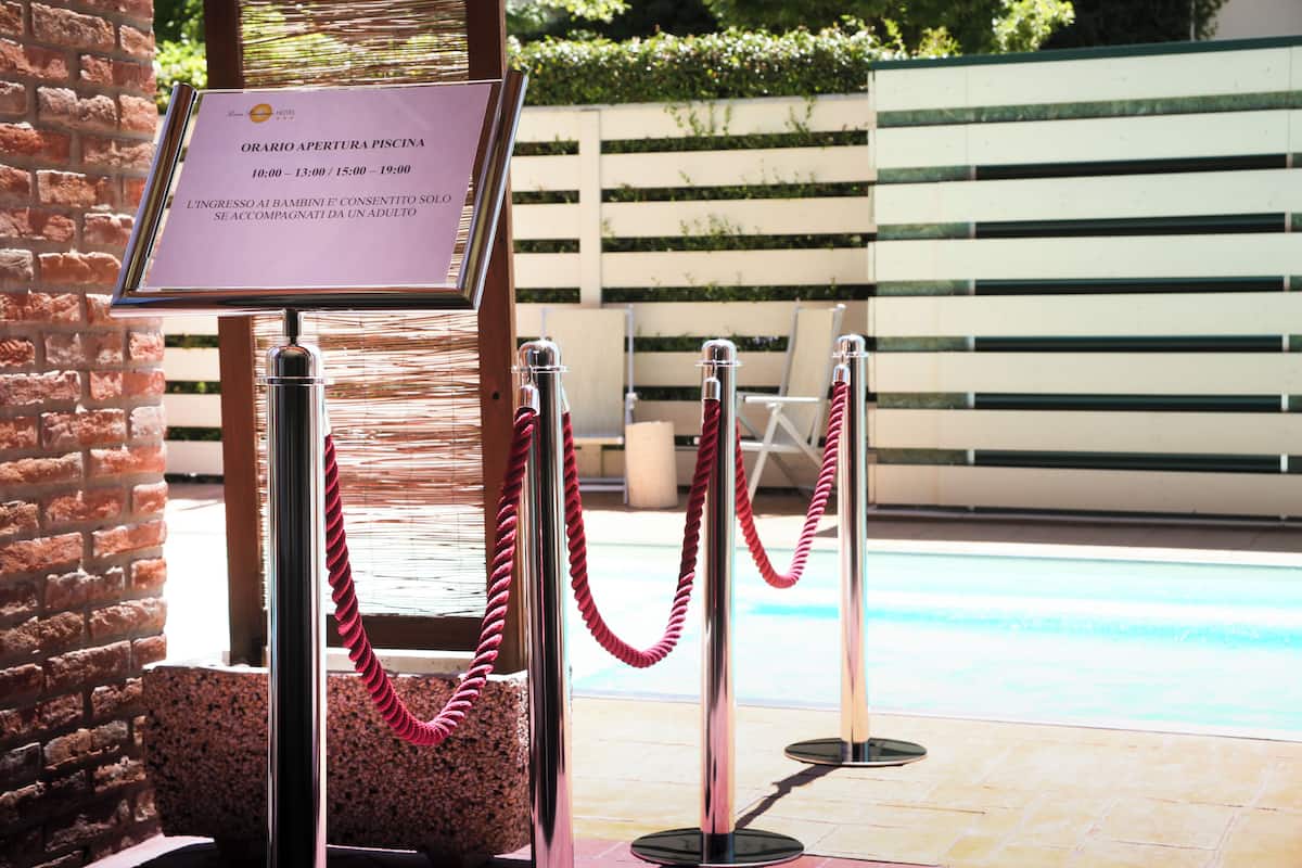 A pool area with a sign indicating pool opening hours and a rope barrier.