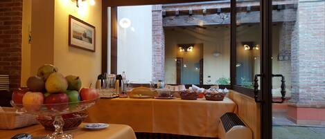Una mesa de comedor dispuesta con frutas, vasos y cubiertos, con vista a un edificio de ladrillo y una ventana.