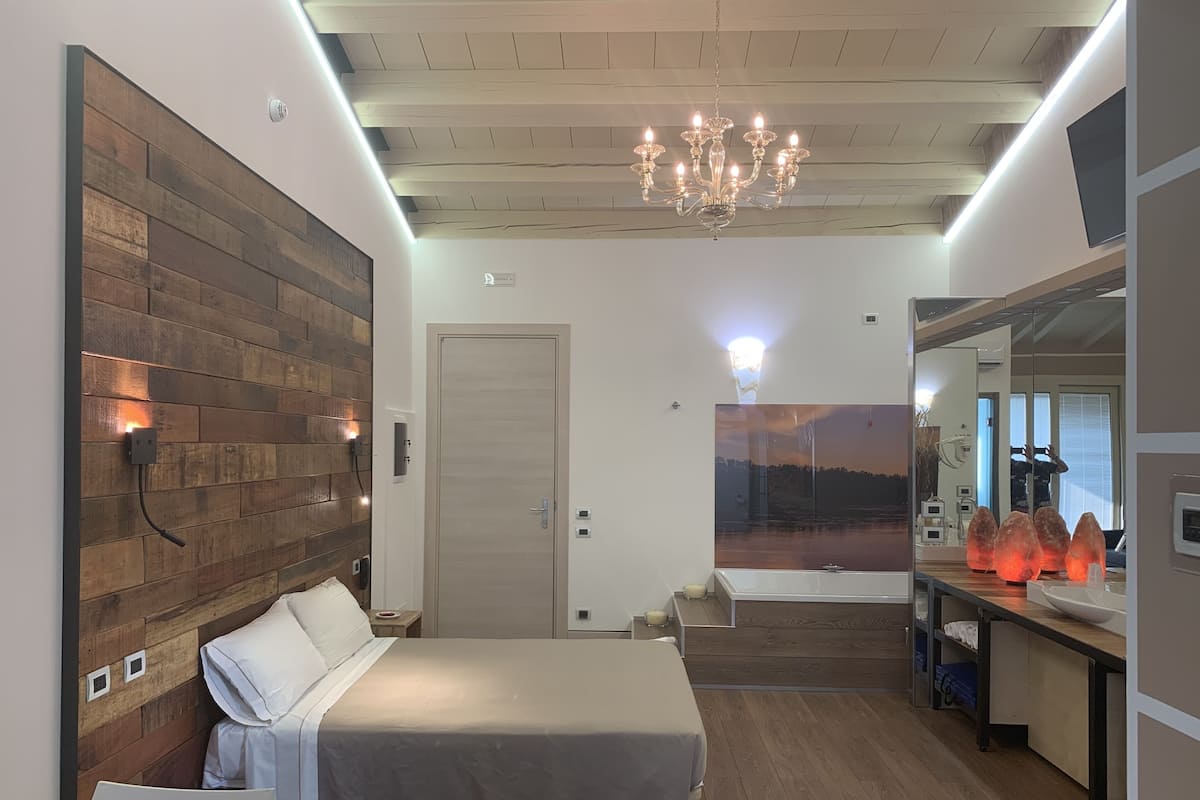 A modern bedroom with a wooden headboard, a large bed, a chandelier, and a painting of a sunset.