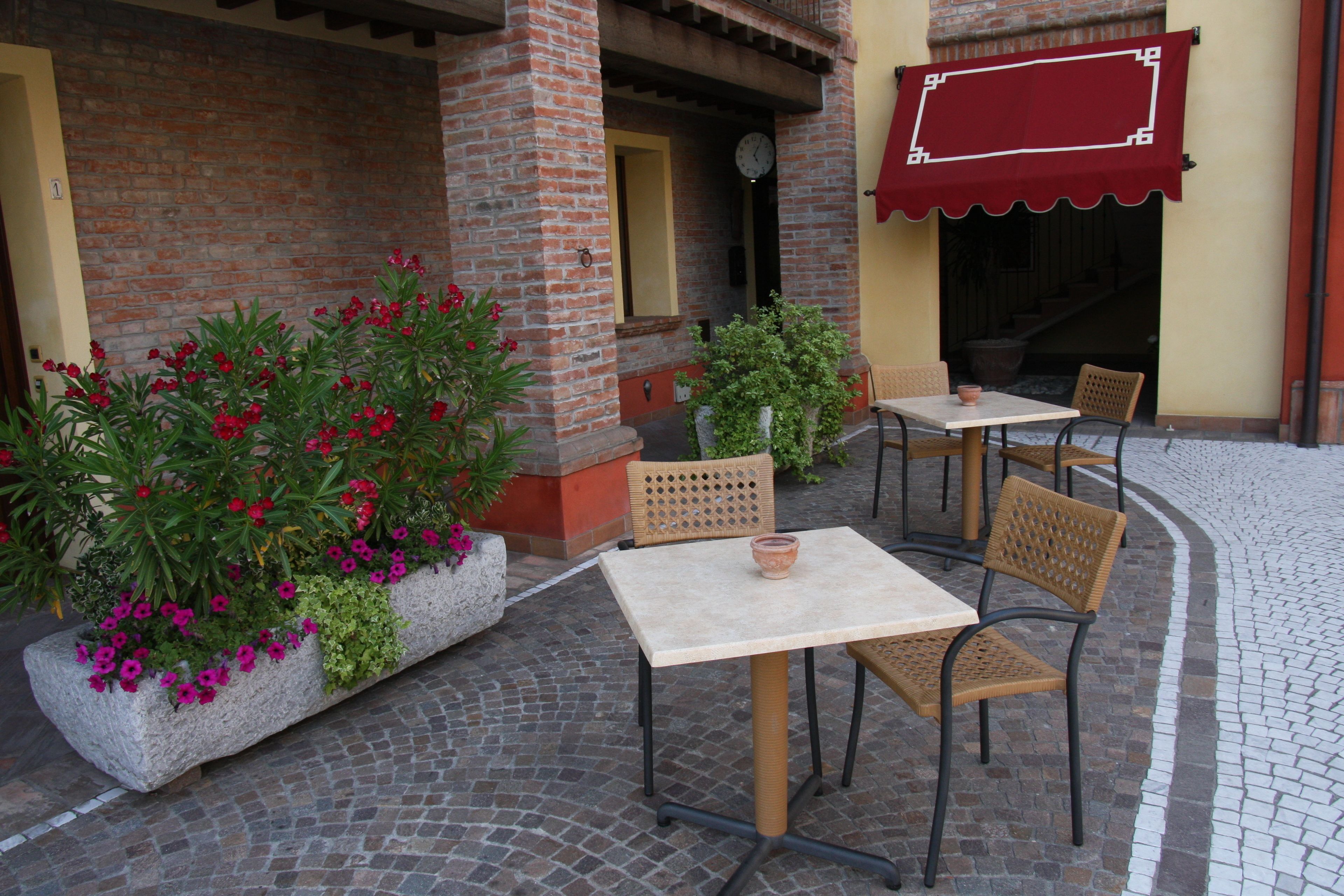 An outdoor seating area with tables and chairs, a brick wall, and potted plants with flowers.