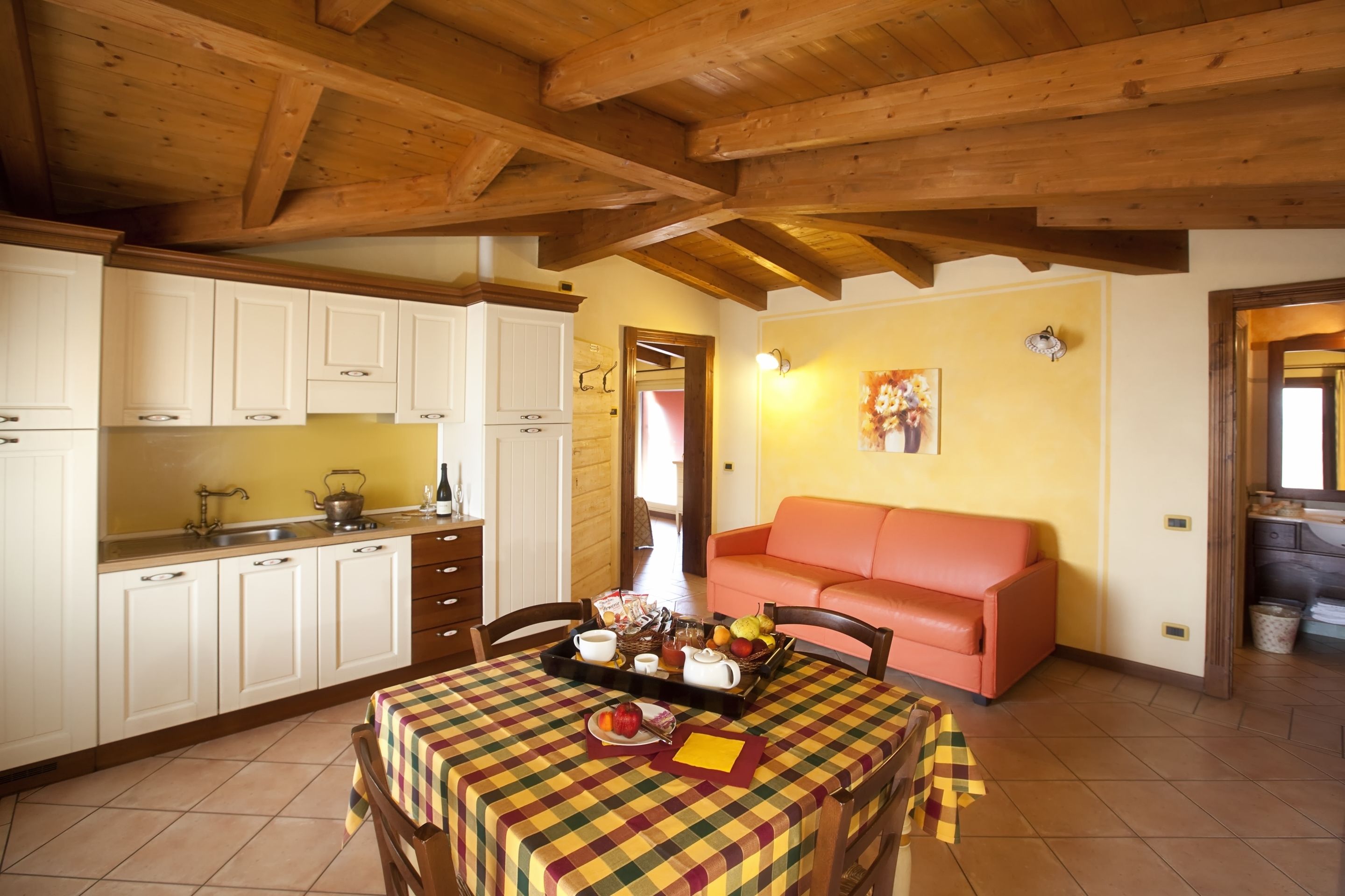 A cozy kitchen with wooden beams, a dining table with a checkered tablecloth, and a red sofa.