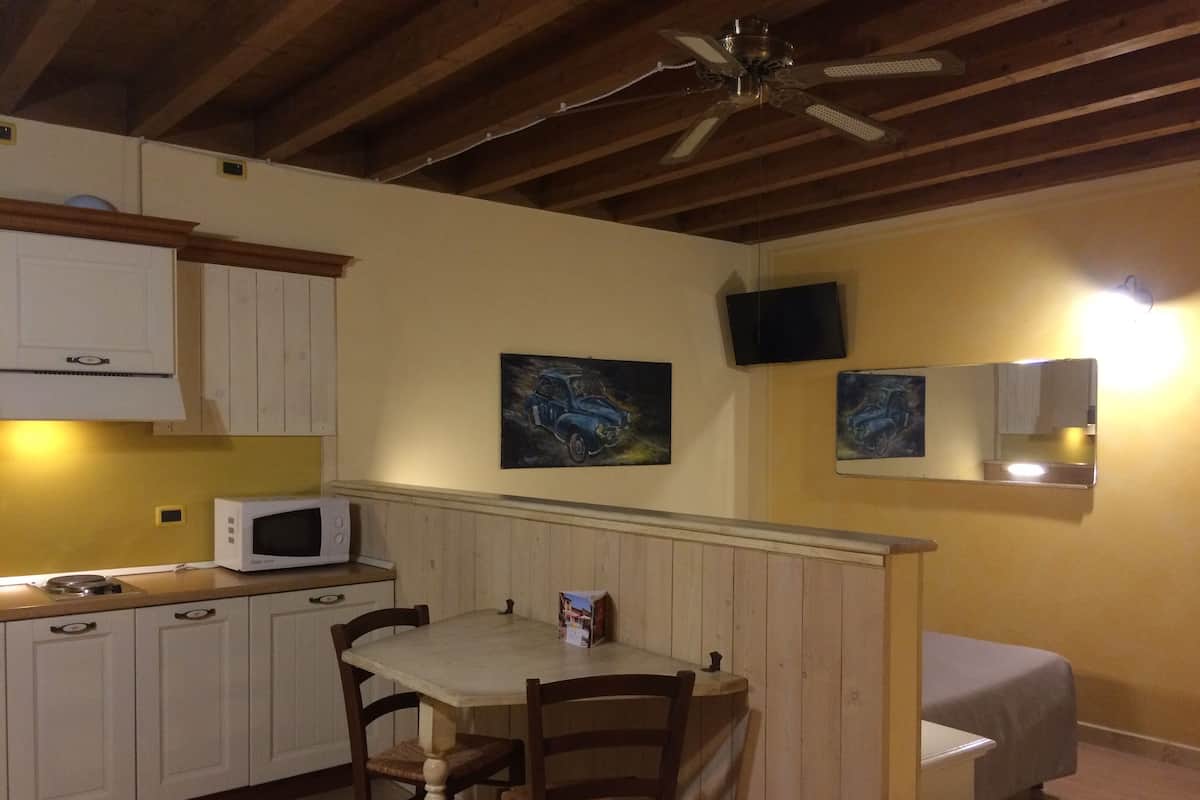 A compact kitchen with white cabinets, a microwave, a dining table with chairs, and a ceiling fan.
