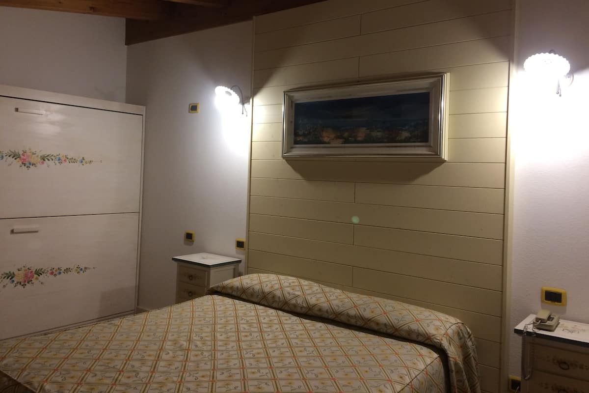 A bedroom with a bed, a dresser, a nightstand, and a wall-mounted painting.
