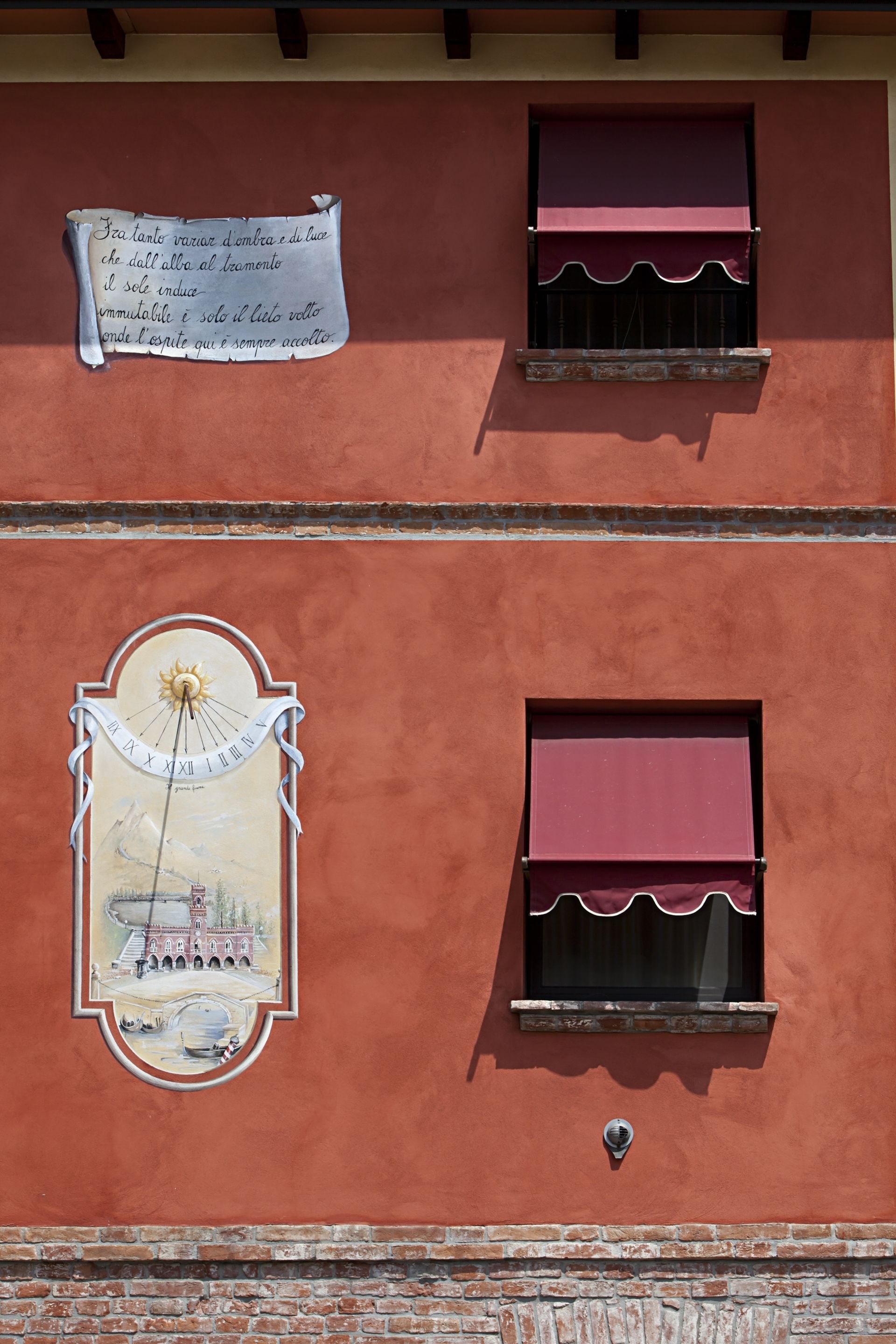 Un edificio con dos ventanas, cada una con un toldo rojo. Una ventana tiene un mural de un sol y un edificio, mientras que la otra muestra un cartel con texto.