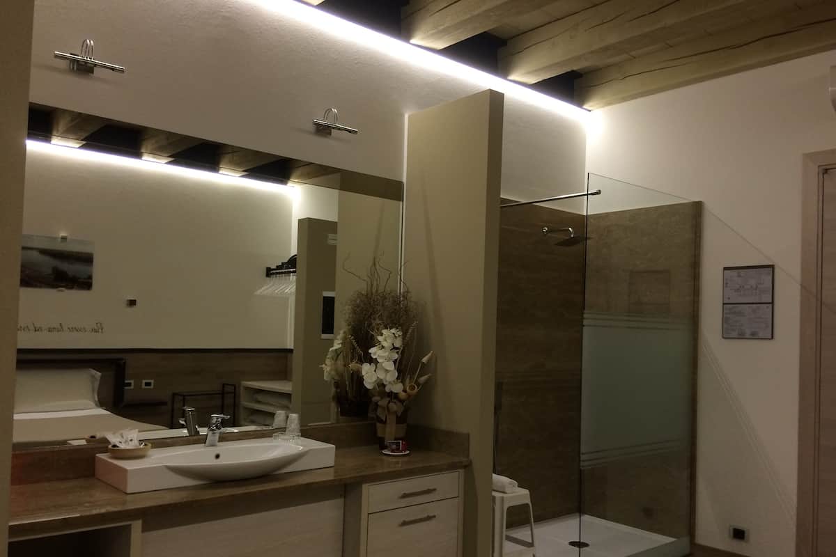 A modern bathroom with a large mirror, a sink, a shower, and a vanity with a towel rack.