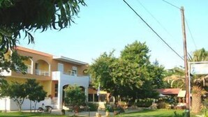 Un edificio de dos pisos con balcón, rodeado de un césped cuidado y árboles.