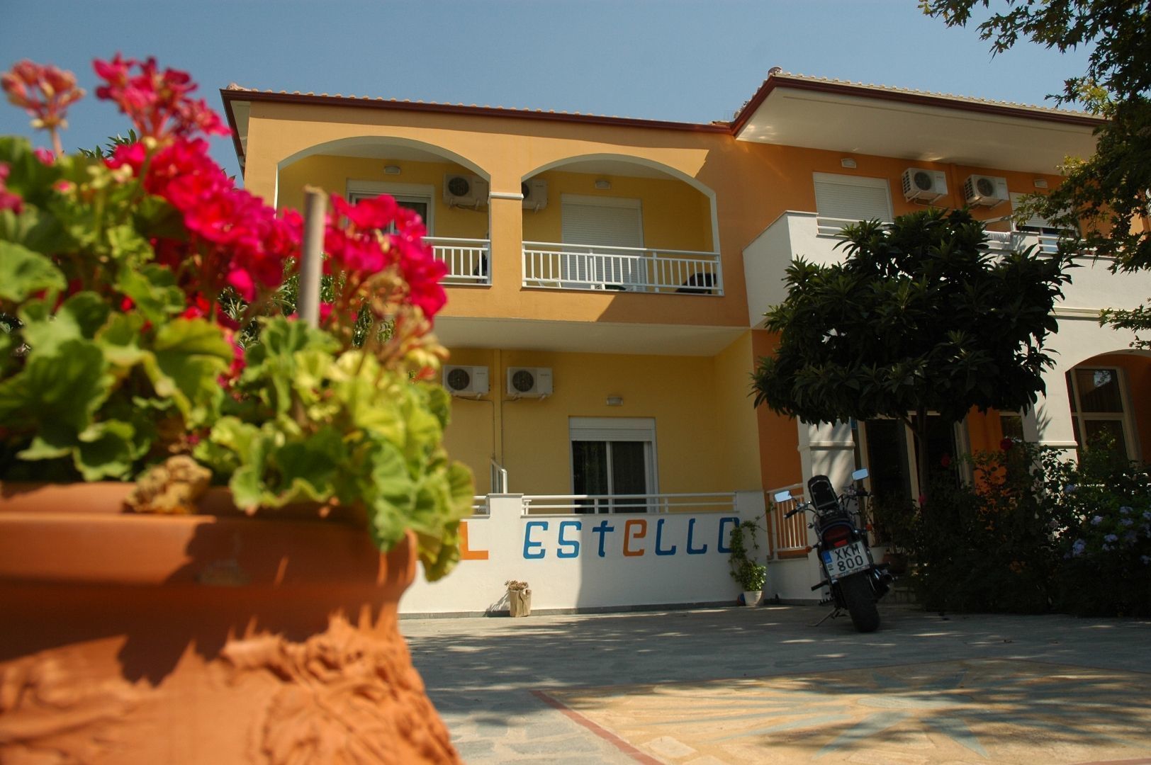 A two-story building with a yellow facade and a sign reading "ESTELLO".
